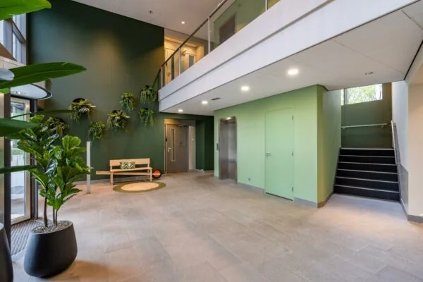 Moderne, groene entreehal aan de Baarnsche Dijk met plantenwand, houten bank en trap naar de bovenverdieping.